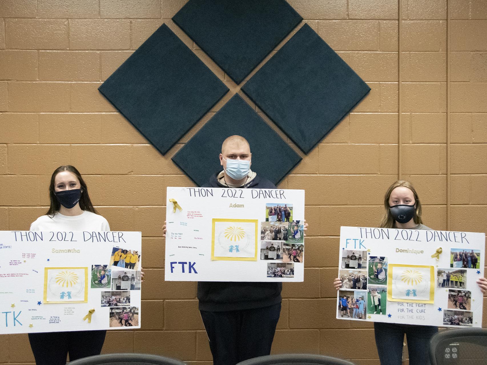 Three students wearing masks stand with 24" x 36" posters with photos and their names on them