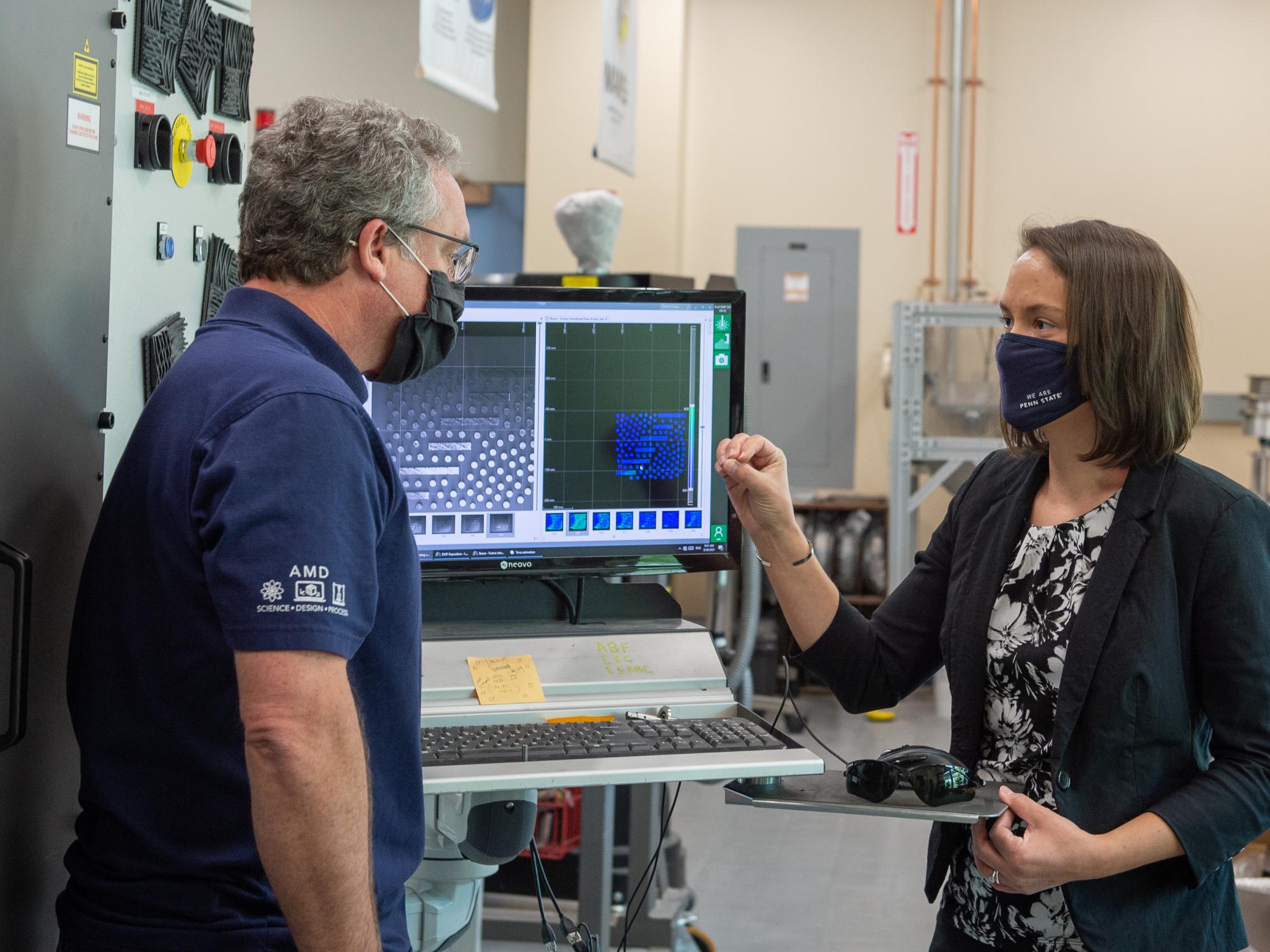 A male and female engineer discuss an additive manufacturing experiment in front of a chrome oven