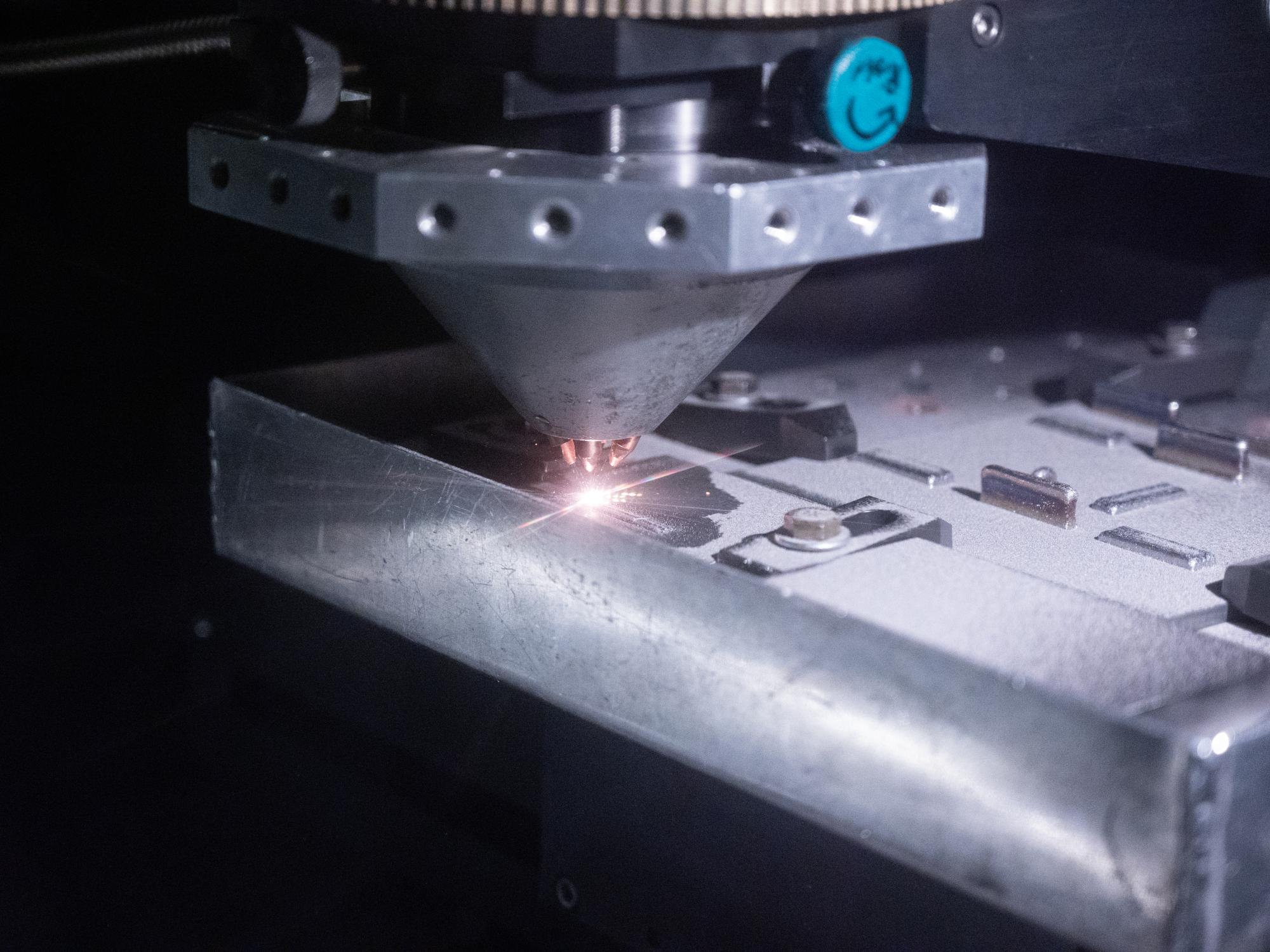close up of a metal nozzle depositing additive material on a surface