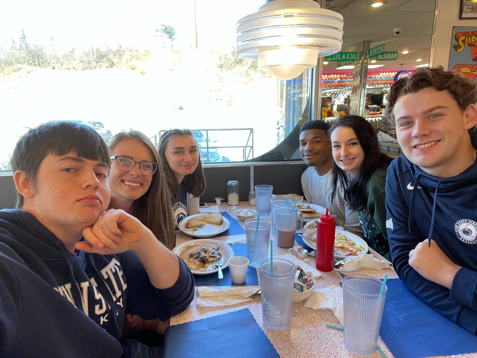 six students sit at a diner table with breakfast food between them