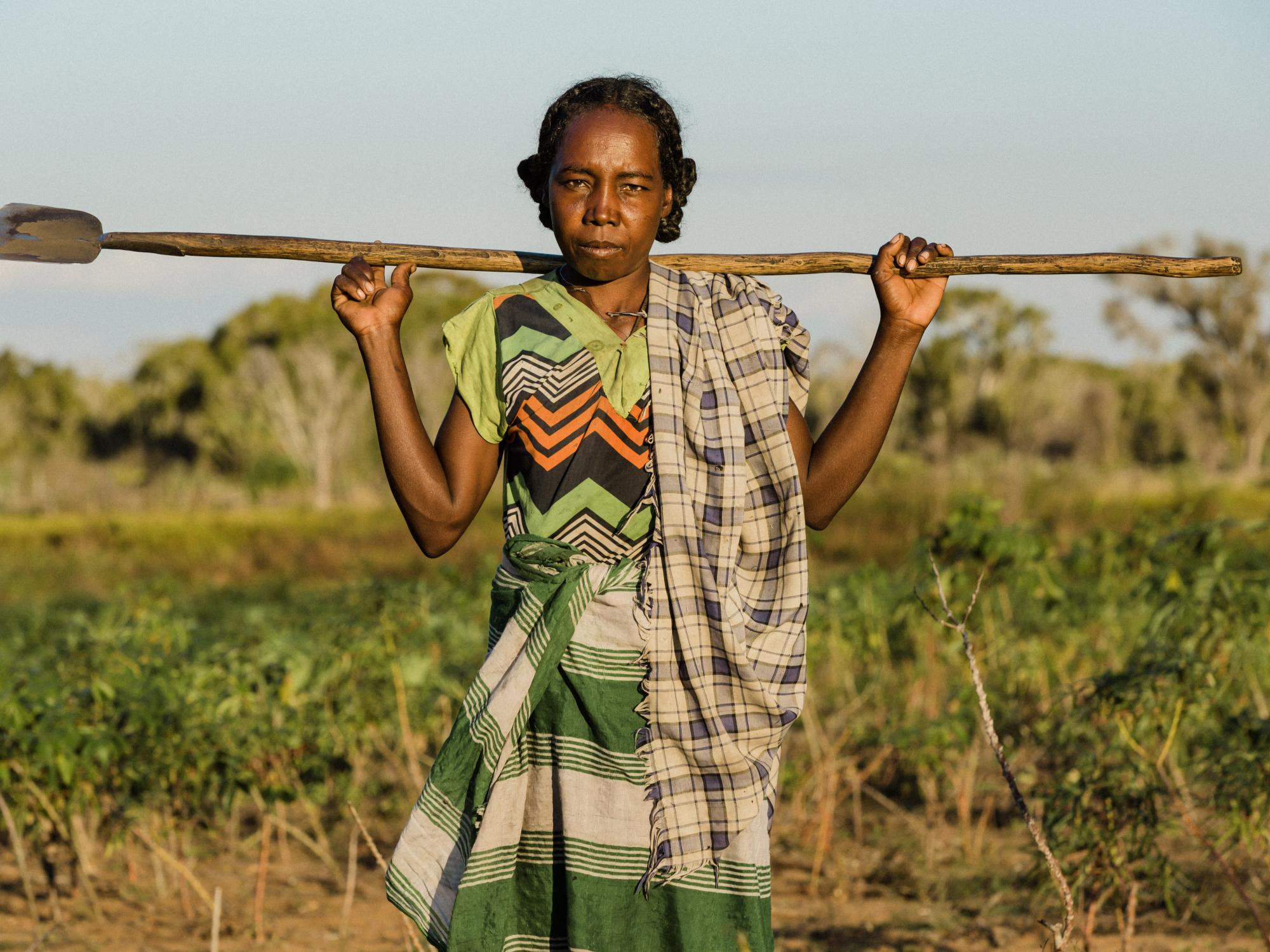 Woman in field holding a hoe across her shoulders
