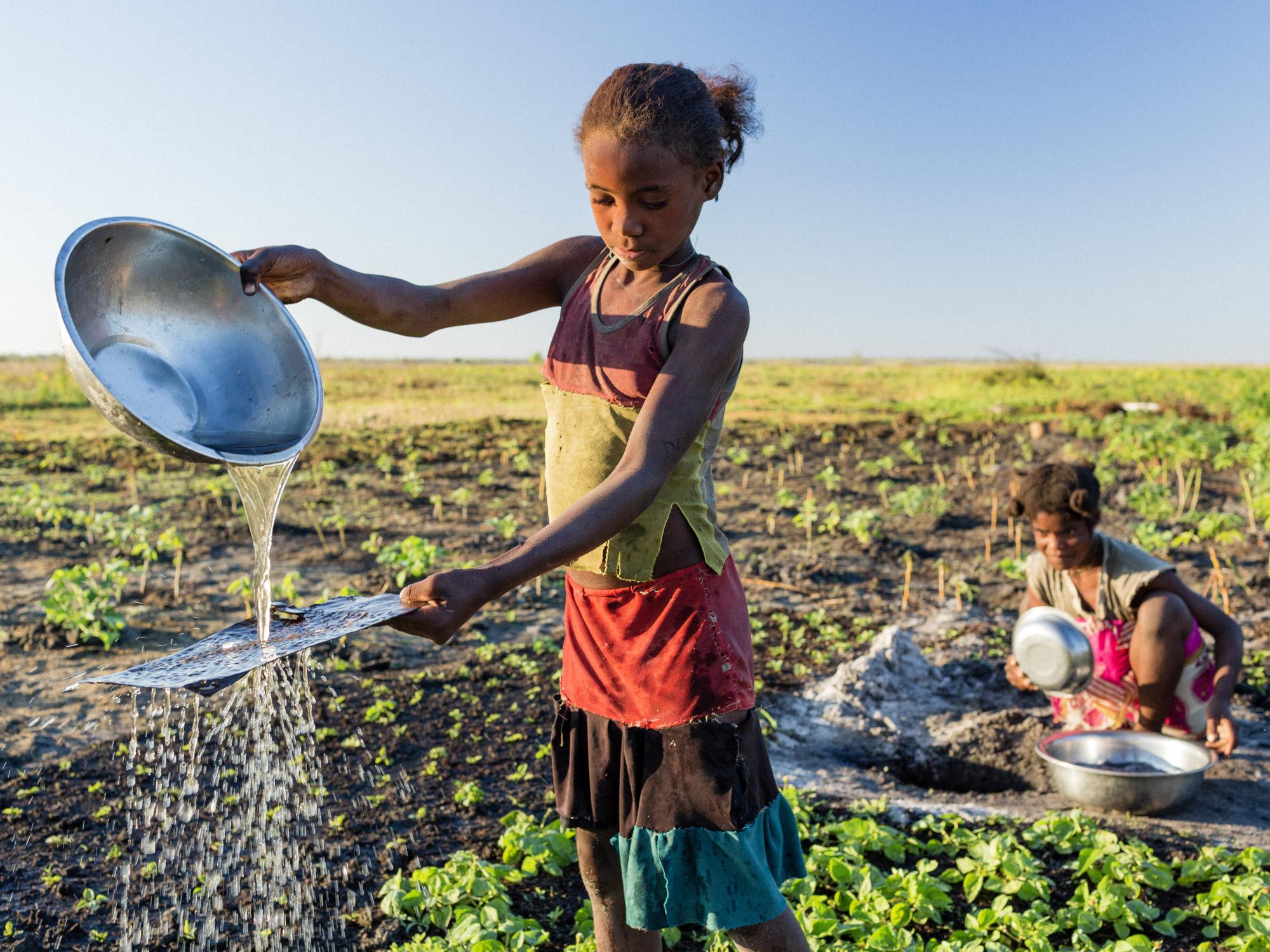 Two girls washing pans in a field