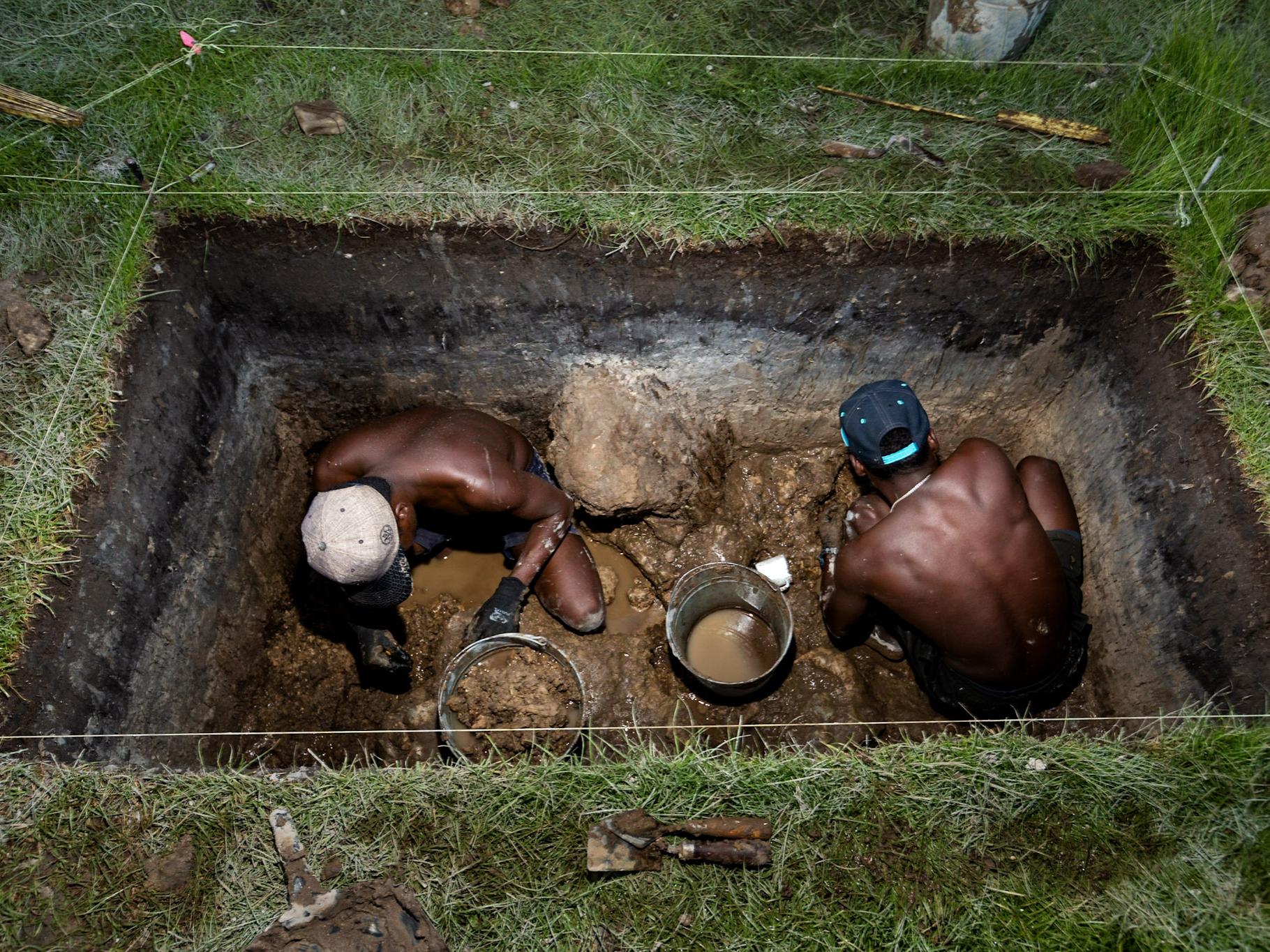 Two men digging for artifacts in a large rectangular pit