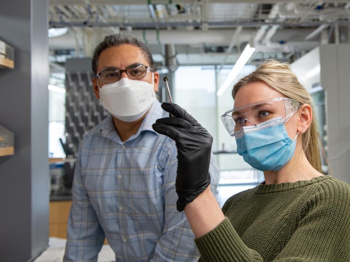 A woman wearing lab glasses holds up tweezers holding a small piece of plastic, as a man looks on.Kelby Hochreither/Penn State