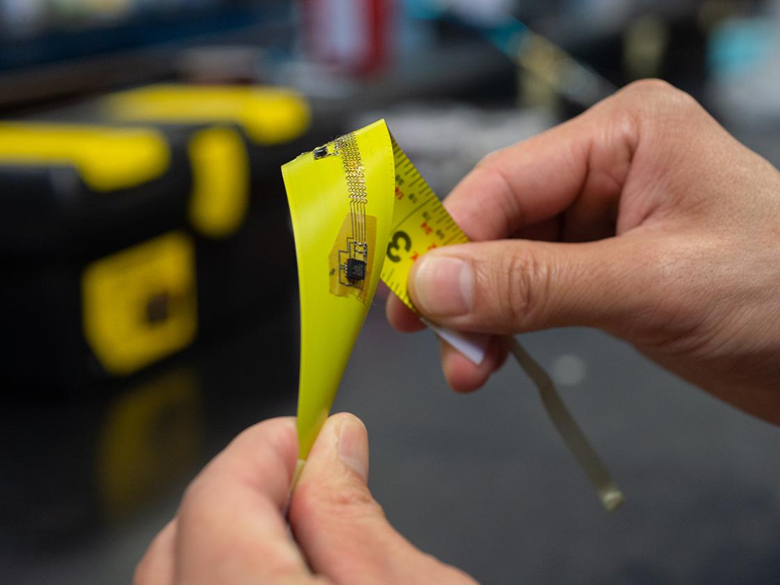 Two hands are pictured twisting a yellow electronic that resembles a tape measure. 
