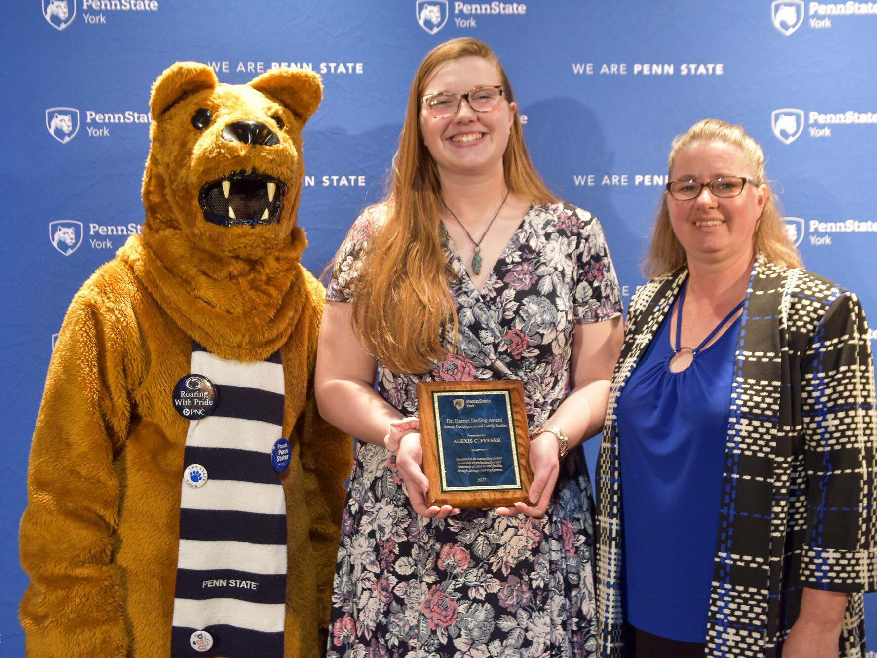 Person dressed in Nittany Lion costume and two femailes with glasses are opart of an award presentation.
