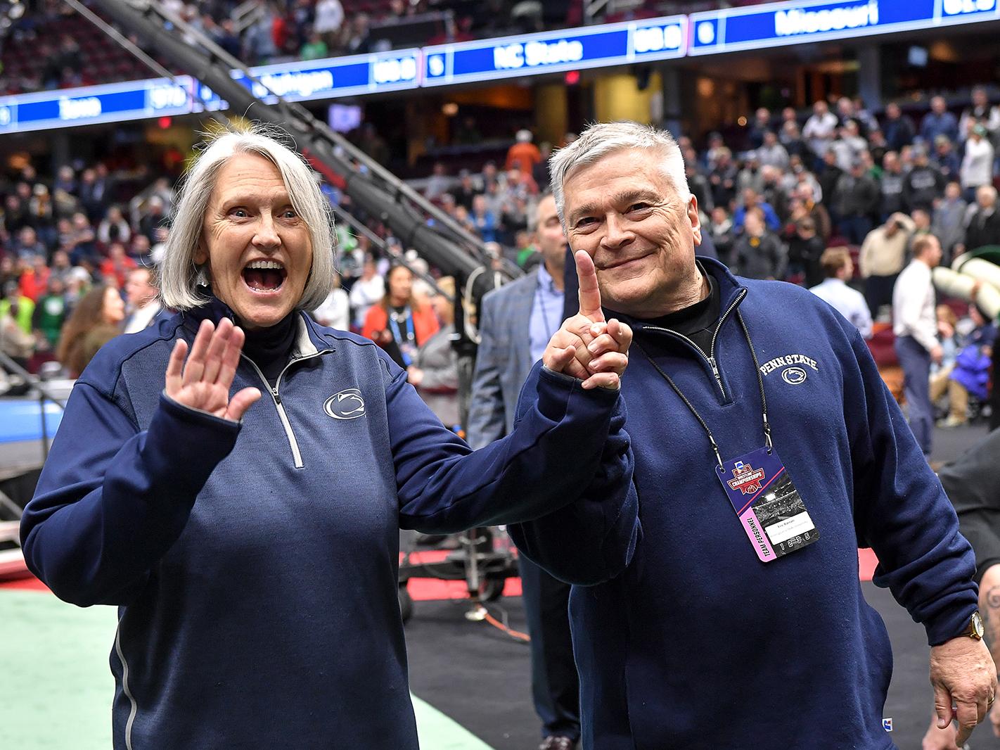 Penn State President Eric Barron holds the hand of his wife, Molly, at the 2018 NCAA Wrestling Championship in Cleveland. Molly is waving and President Barron has is raising a single finger to celebrate the wrestling team's national championship.