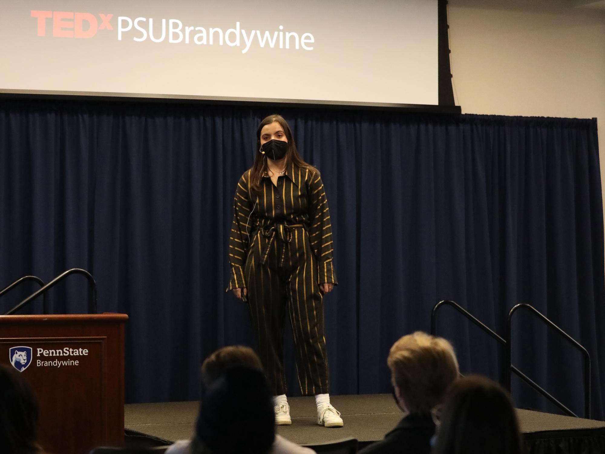 A female student stands on a stage speaking to an audience.