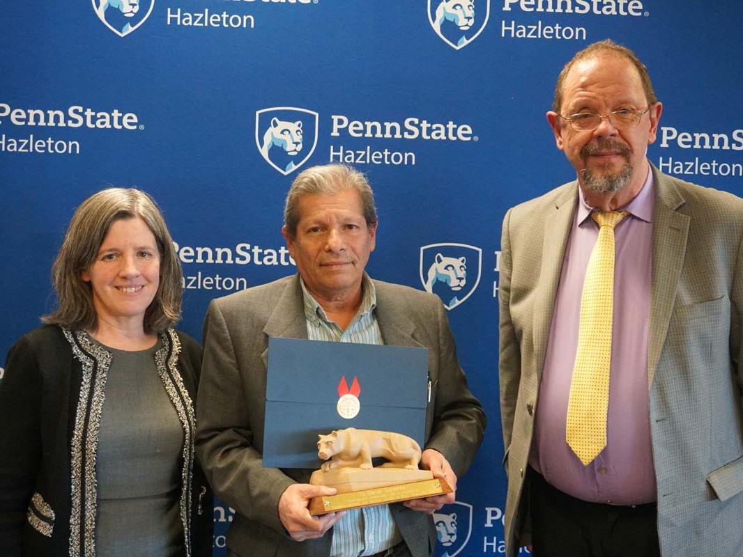 Man standing with miniature Nittany Lion statue and certificate with man and women at his side.