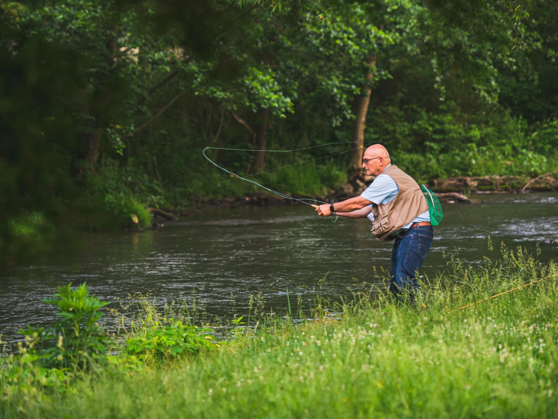 Richard Roush, dean of the College of Agricultural Sciences, casts his fishing line into a creek from the bank beside the water
