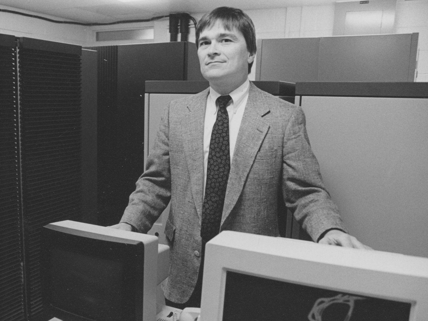 A black and white photo of Eric Barron standing next to computers.