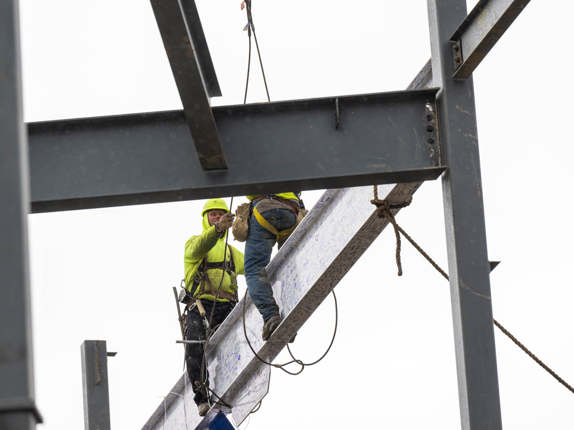 Two steelworkers set a beam in place at the site of Penn State Behrend's new Erie Hall.