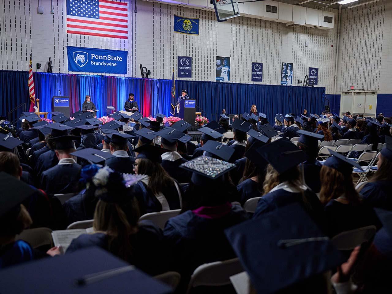 Campus gym filled with graduates wearing caps and gowns.