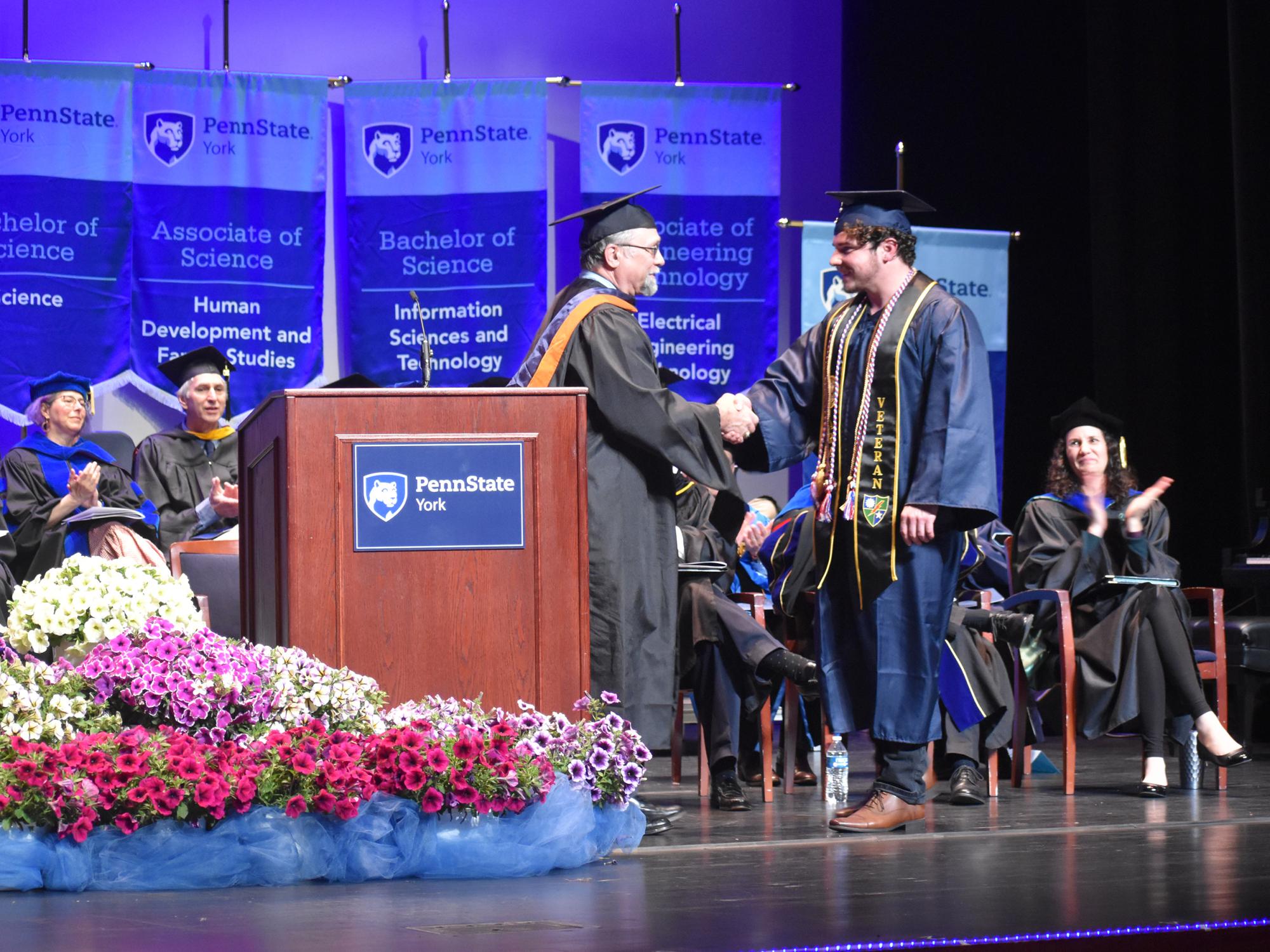 Faculty member in full academic regalia congratulating a student-veteran cap and gown at commencement