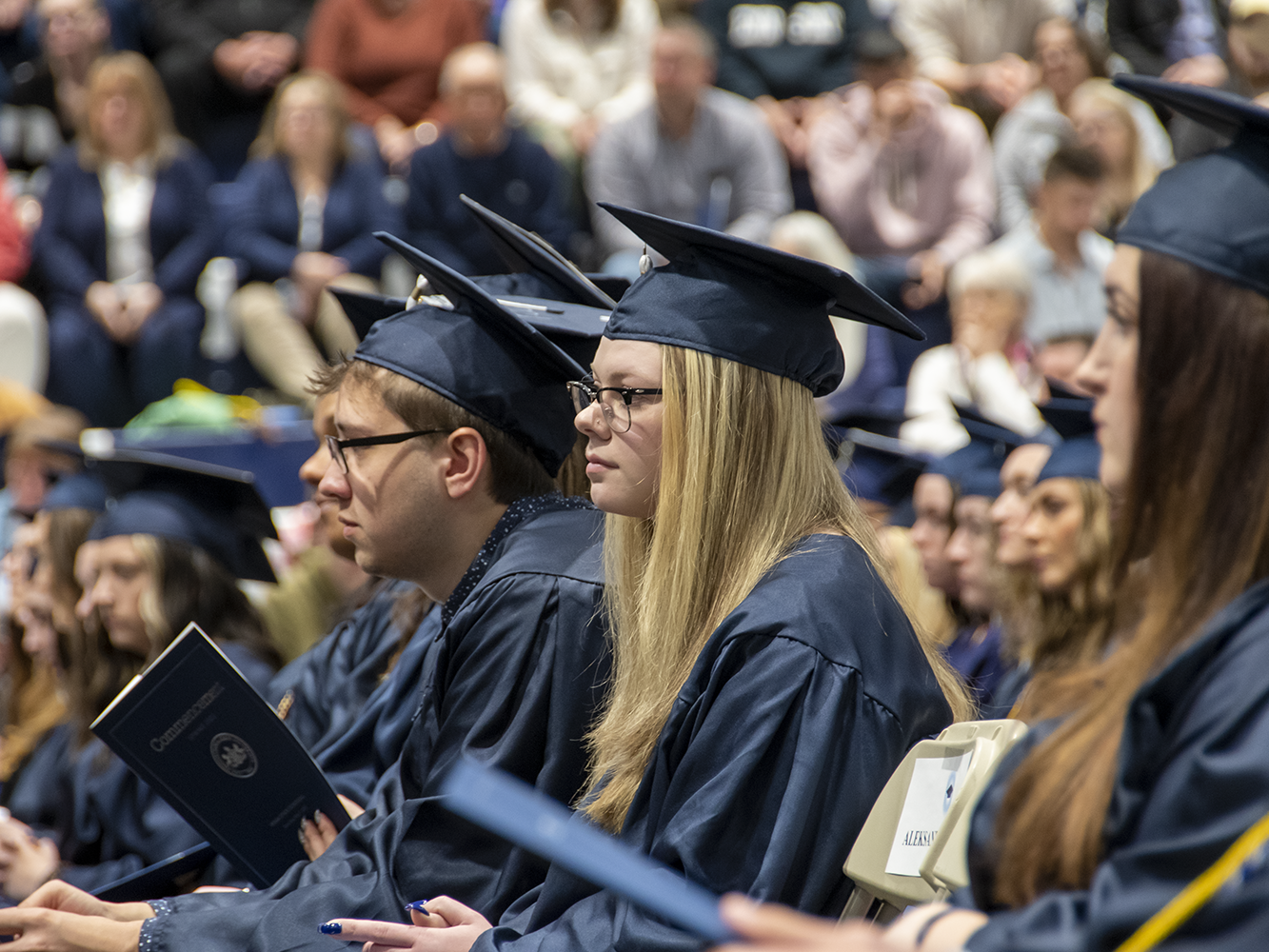 A row of graduates with audience member in the background.