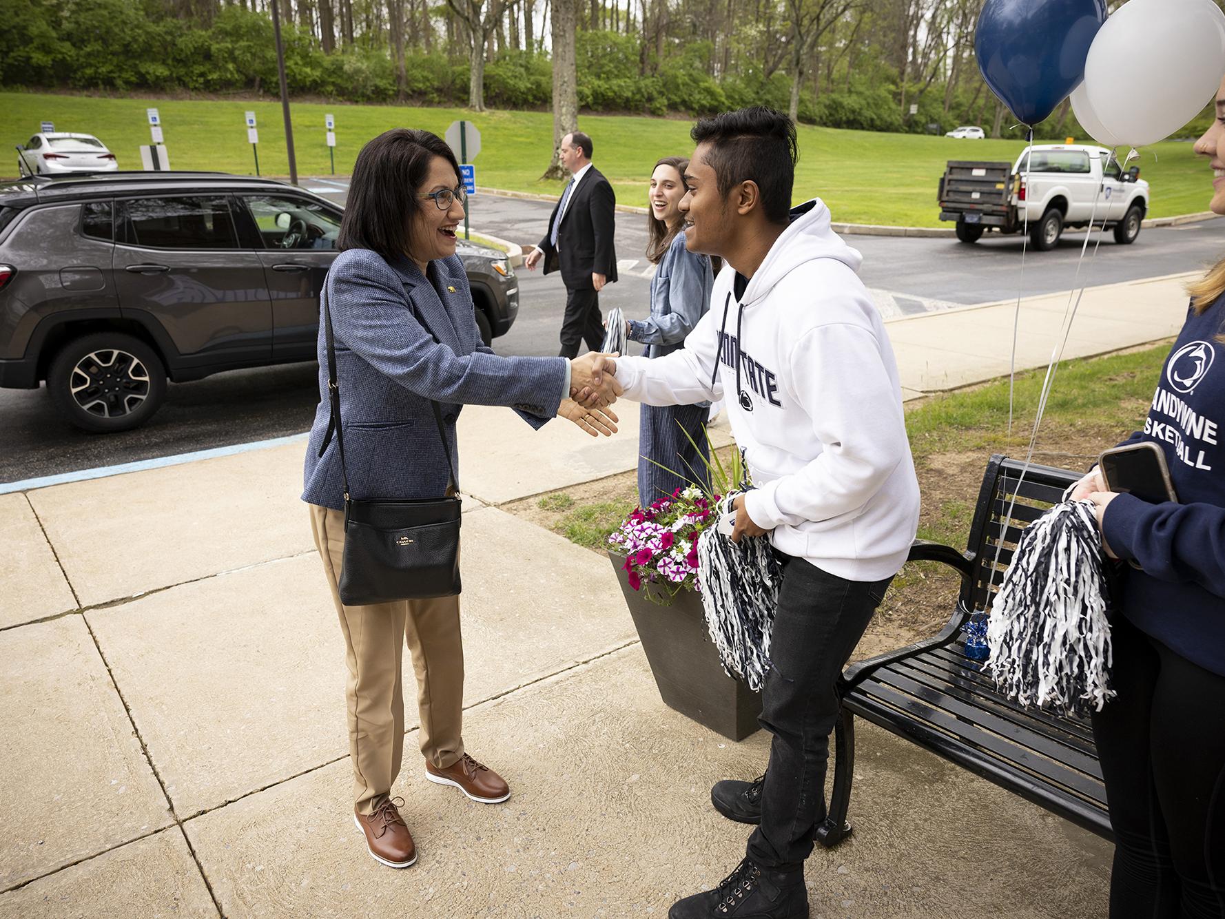 A woman shakes the hand of a male student.