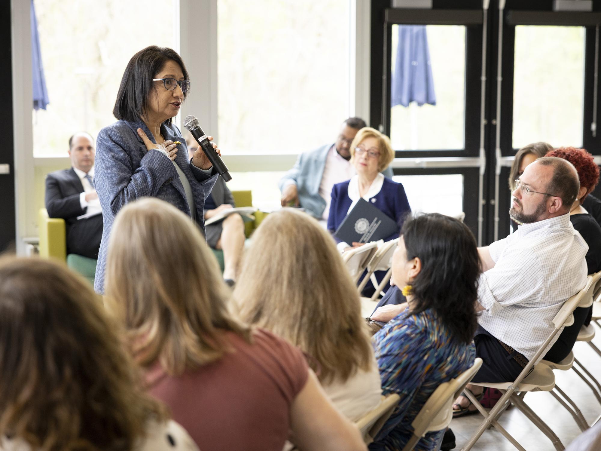 A woman stands and speaks to a group seated.
