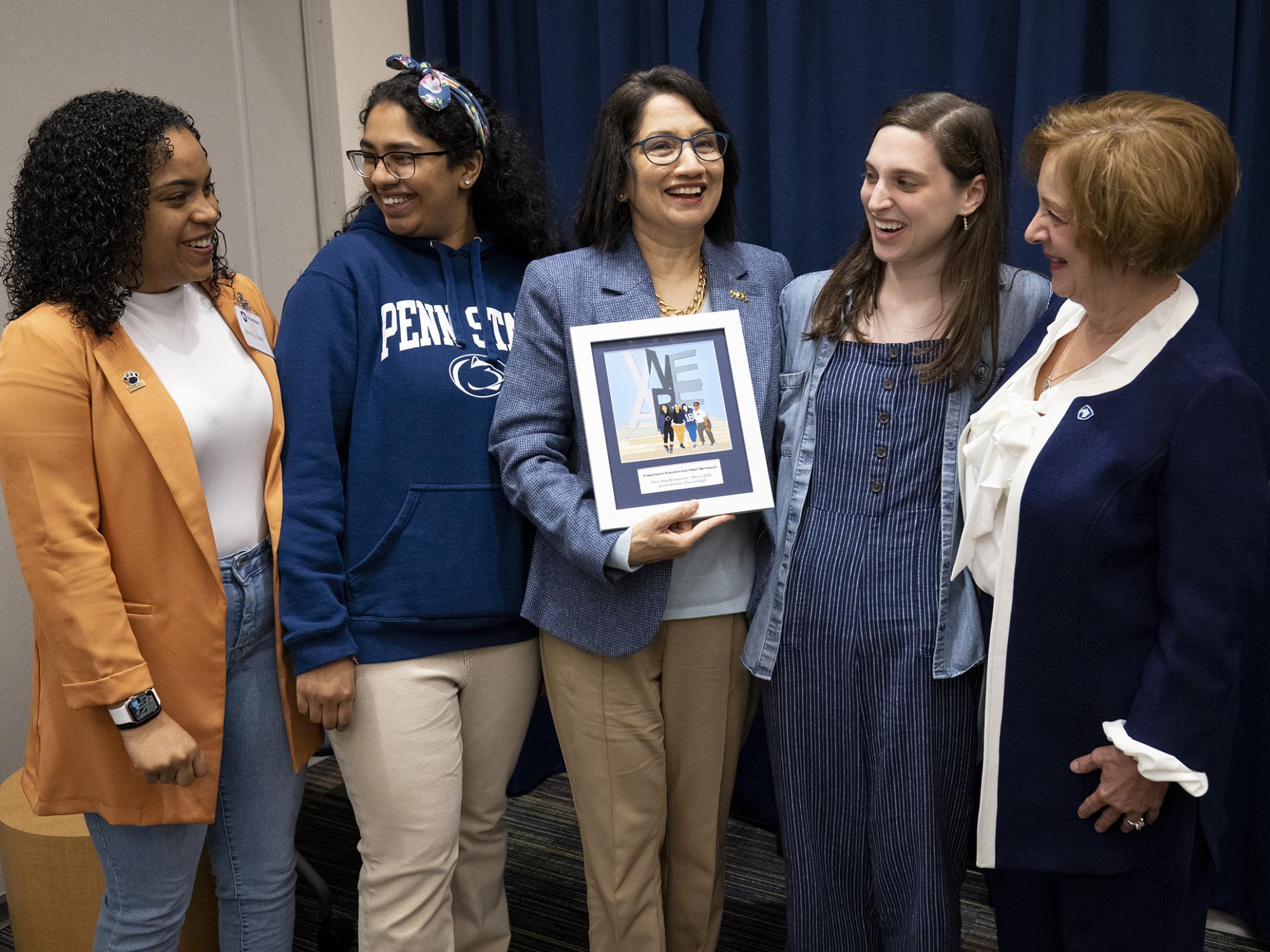 A group of five woman standing with one holding an artwork.