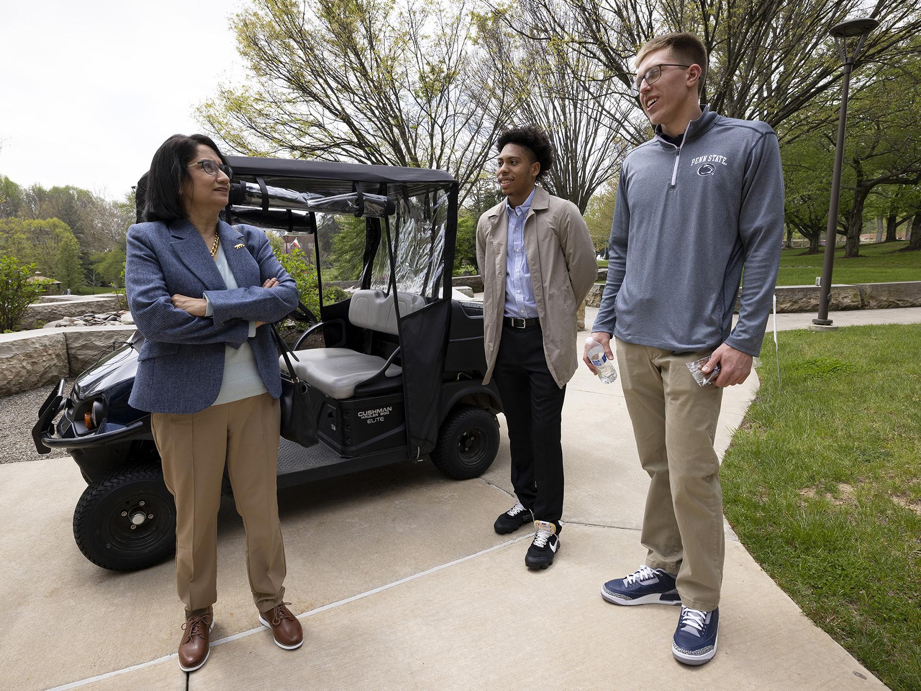 A woman and two men stand next to a golf cart.