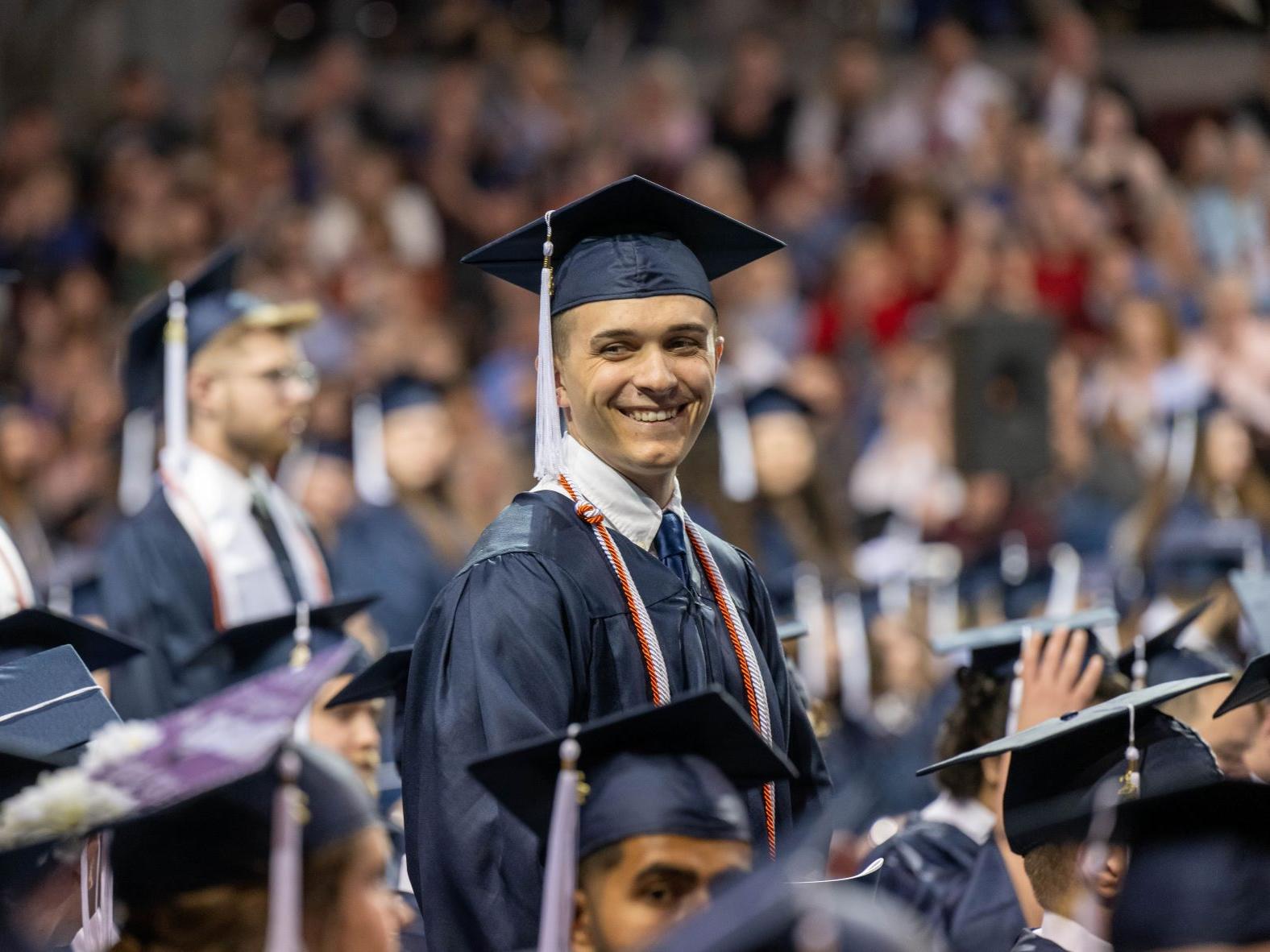 A graduate stands and smiles during Penn State Behrend's spring commencement ceremony.