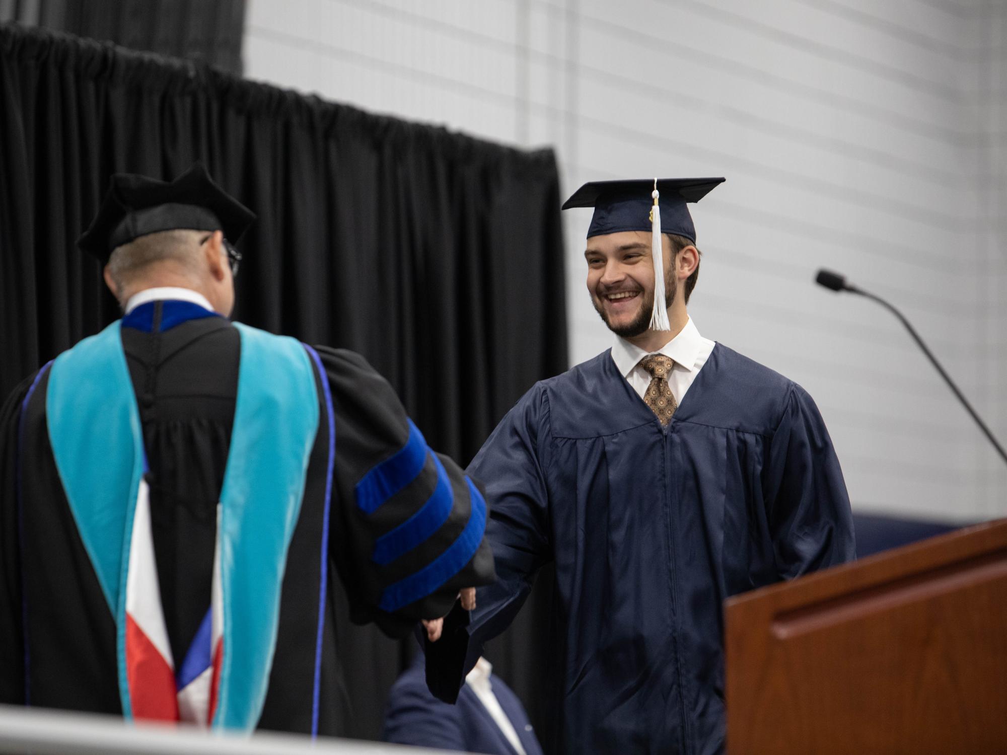 Graduate shakes hands with chancellor and smiles