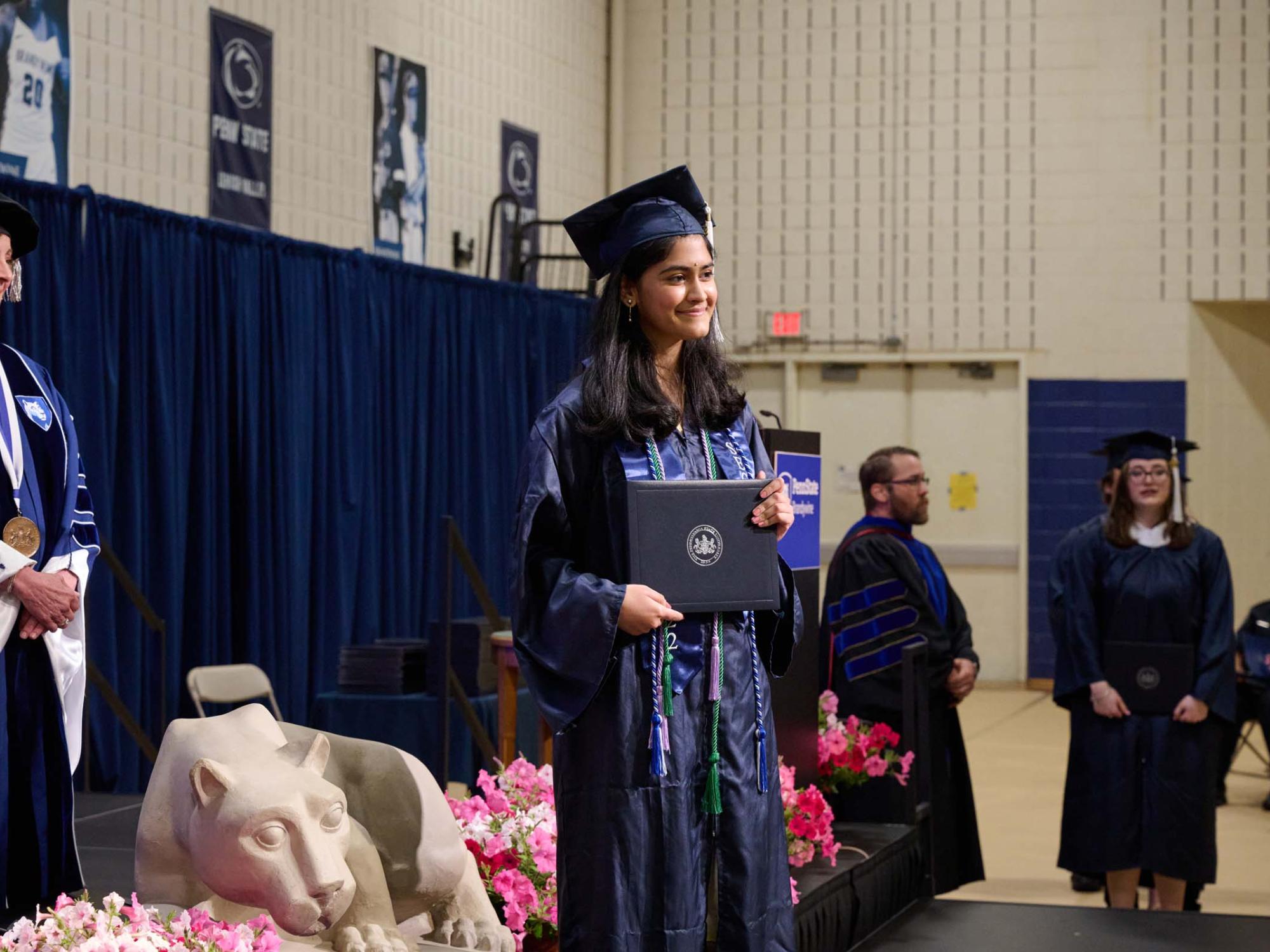 A woman stands on a stage holding a diploma.