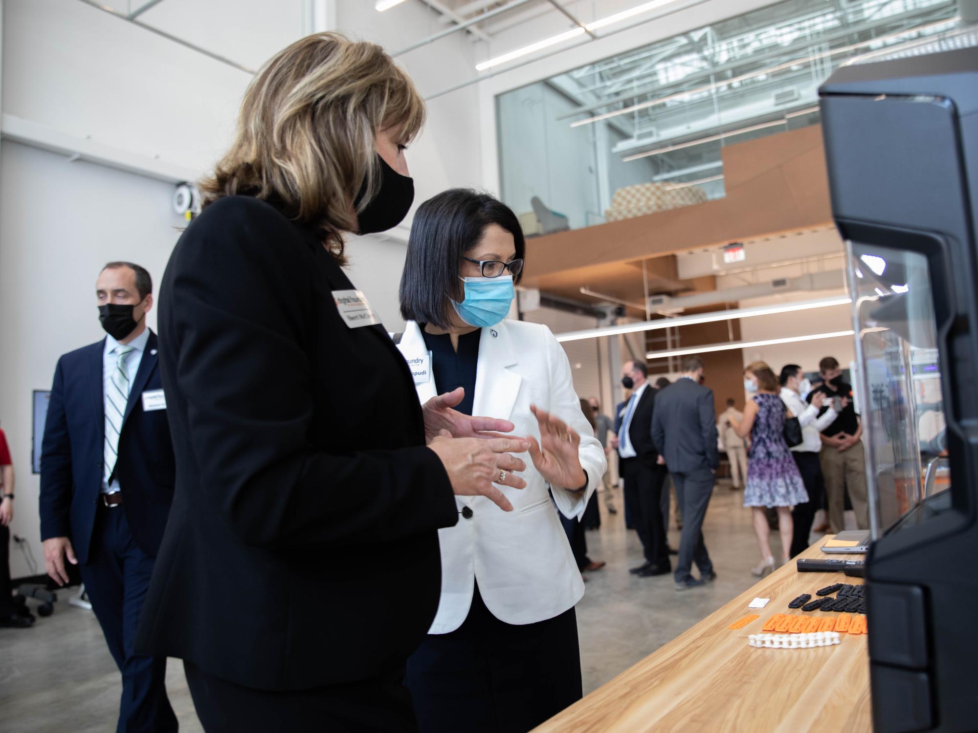 Two individuals stand in front of a 3D printer