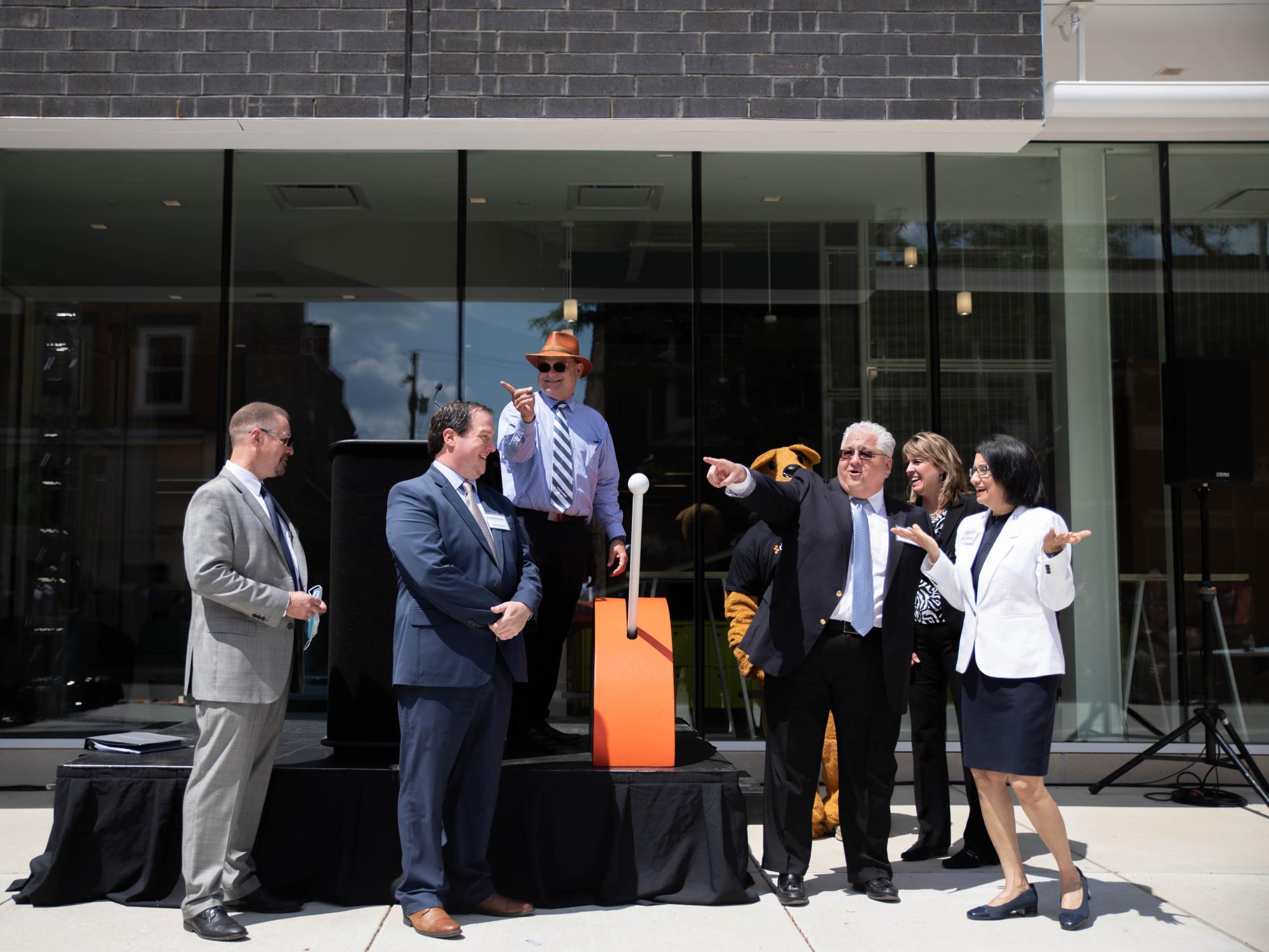 Six individuals stand on and by a stage outside a building
