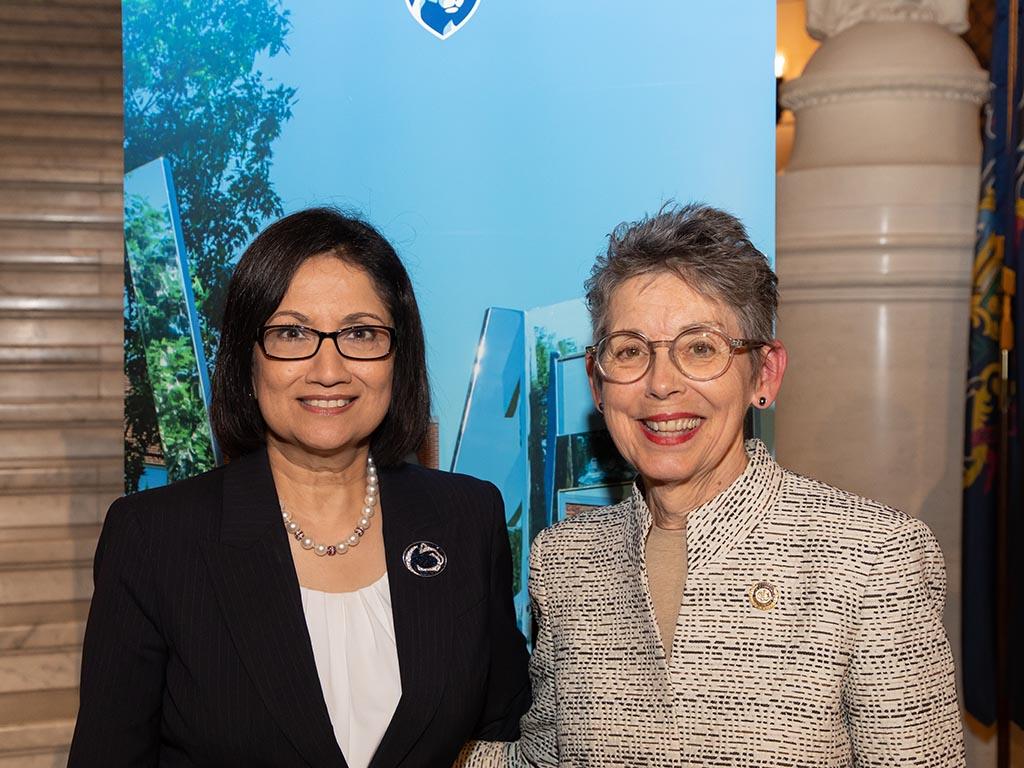 two women stand in front of Penn State banner