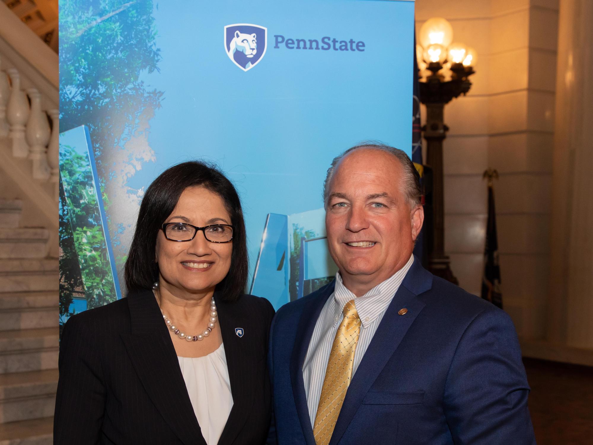 man and woman standing in front of a Penn State banner