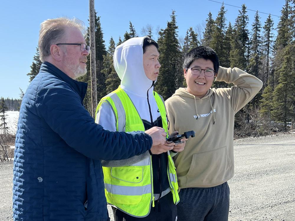 older man with glasses helps two younger men use a remote control  