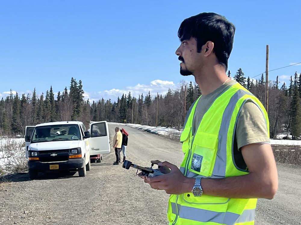 young bearded man in safety vest operates a remote control along a country road