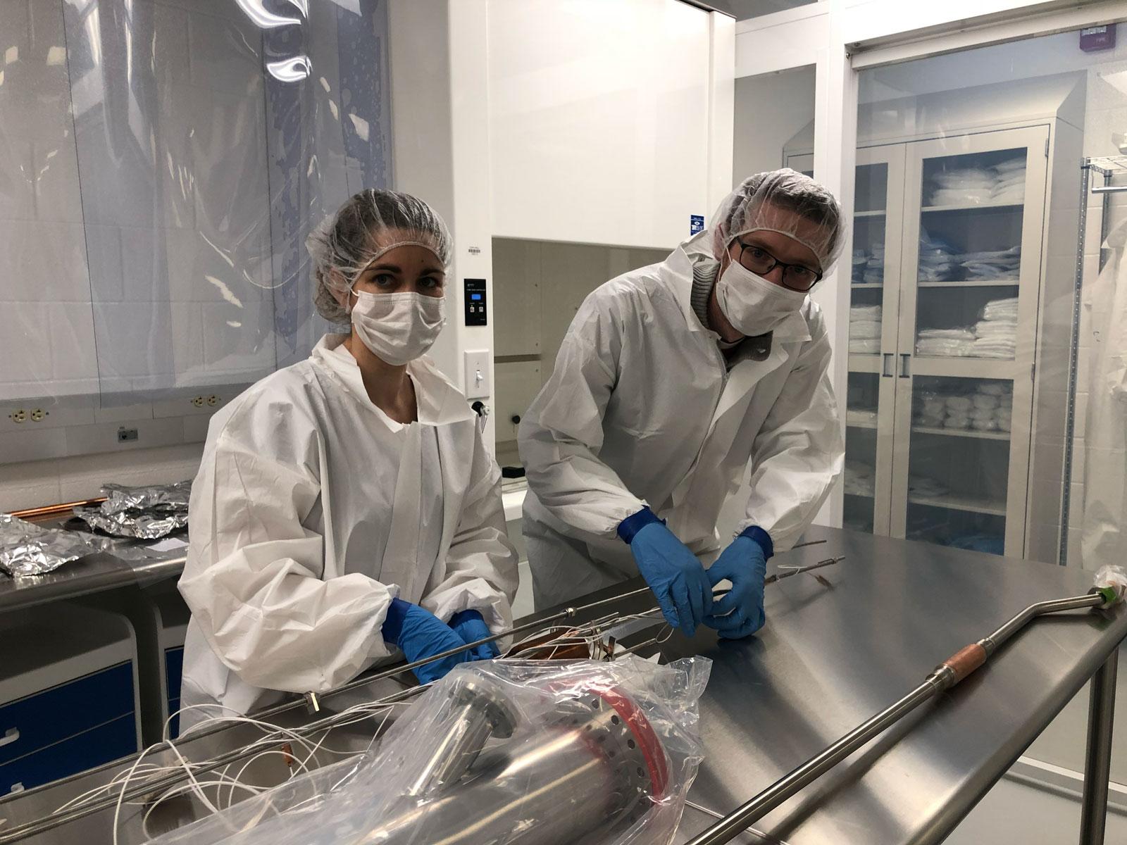 two people in cleanroom suits work at metal table