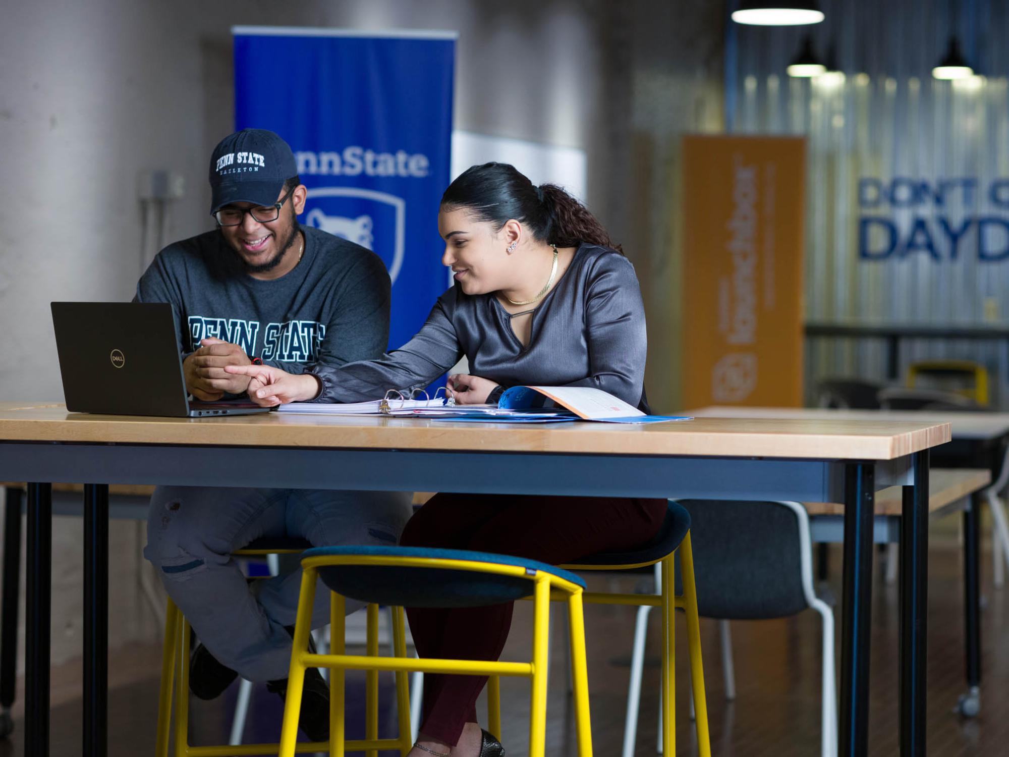 Two students seated at a desk working from a laptop computer.