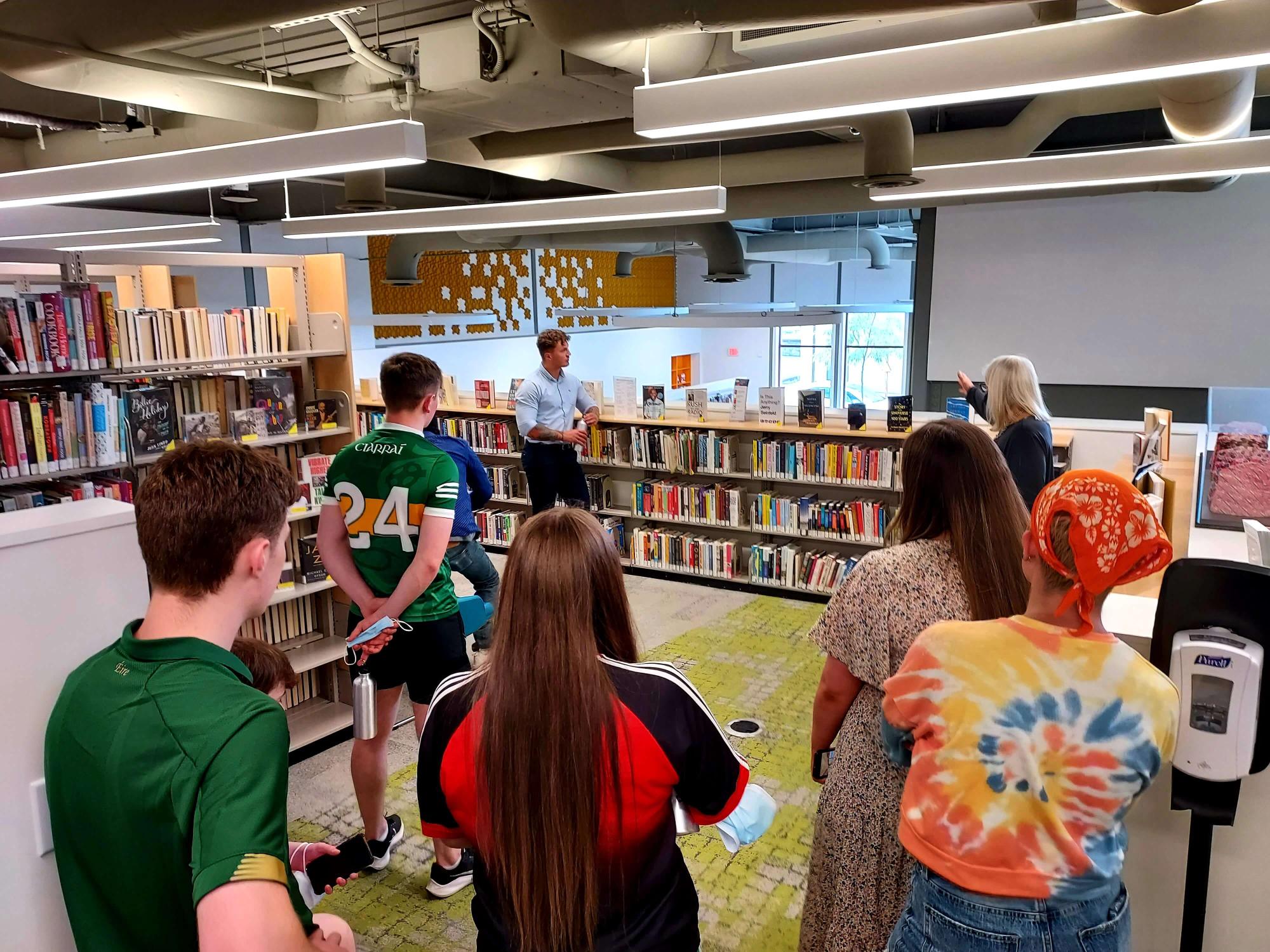 People standing in front of the book stacks in a library.