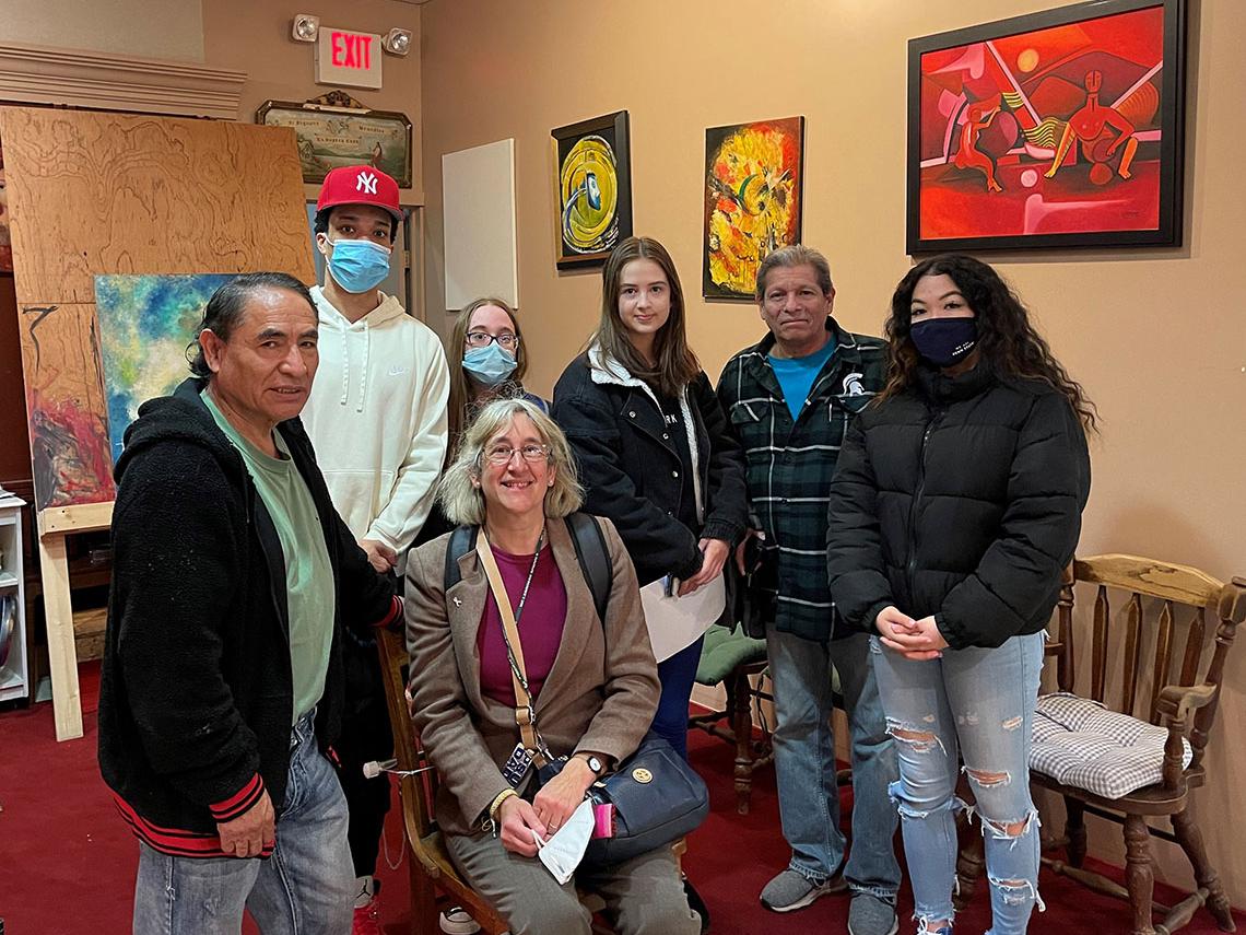 A group of students and teachers standing with an artist in a room full of the artist's paintings.