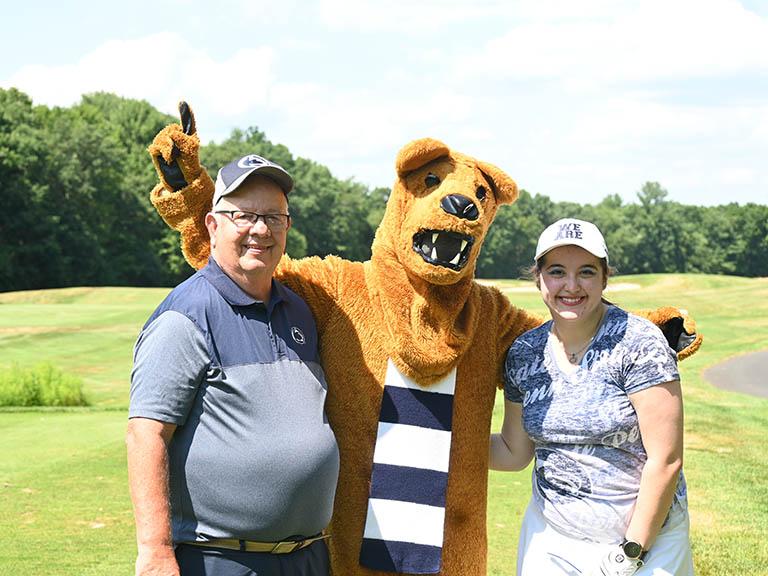 Two people standing with the Nittany Lion.
