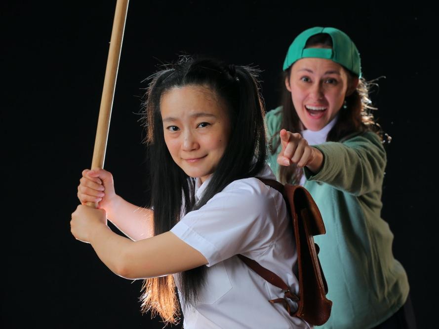 A girl holds a baseball bat ready to swing while a girl stands behind her and cheers her on.