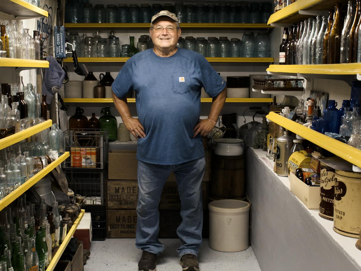 Man stands among shelves of glass bottles and other unearthed treasures
