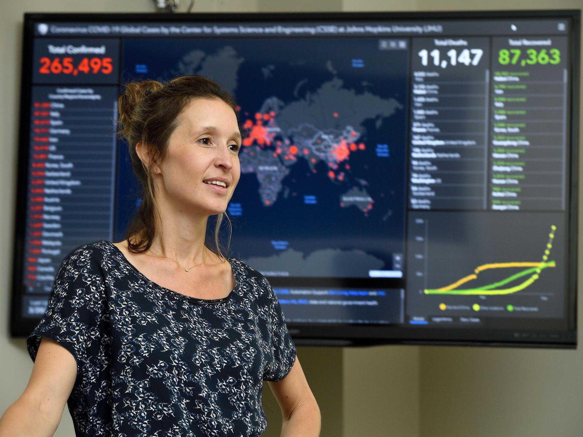 Scientist stands before screen showing geospatial data