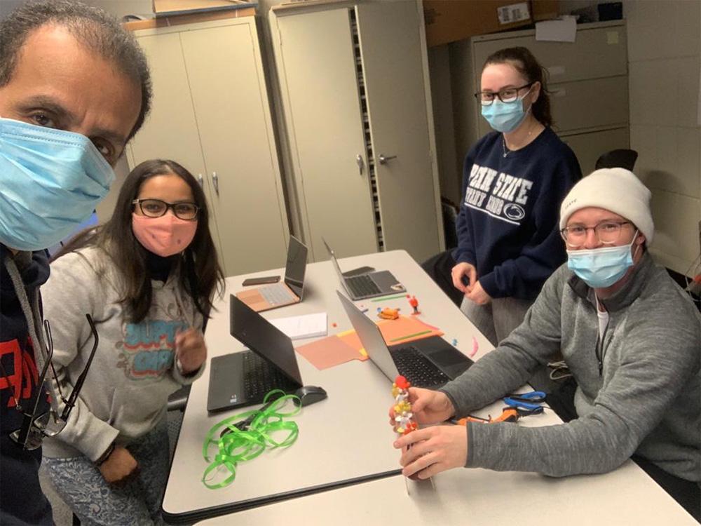 A group of students wearing masks sits around a lab table. 