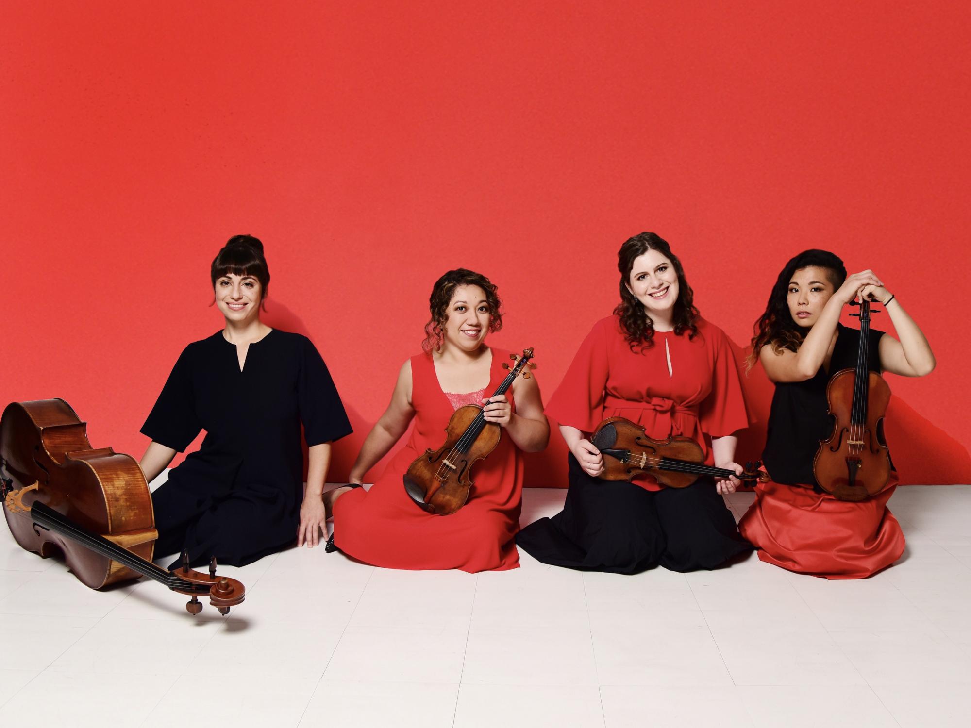 Four woman musicians sit in a row and hold their stringed instruments.