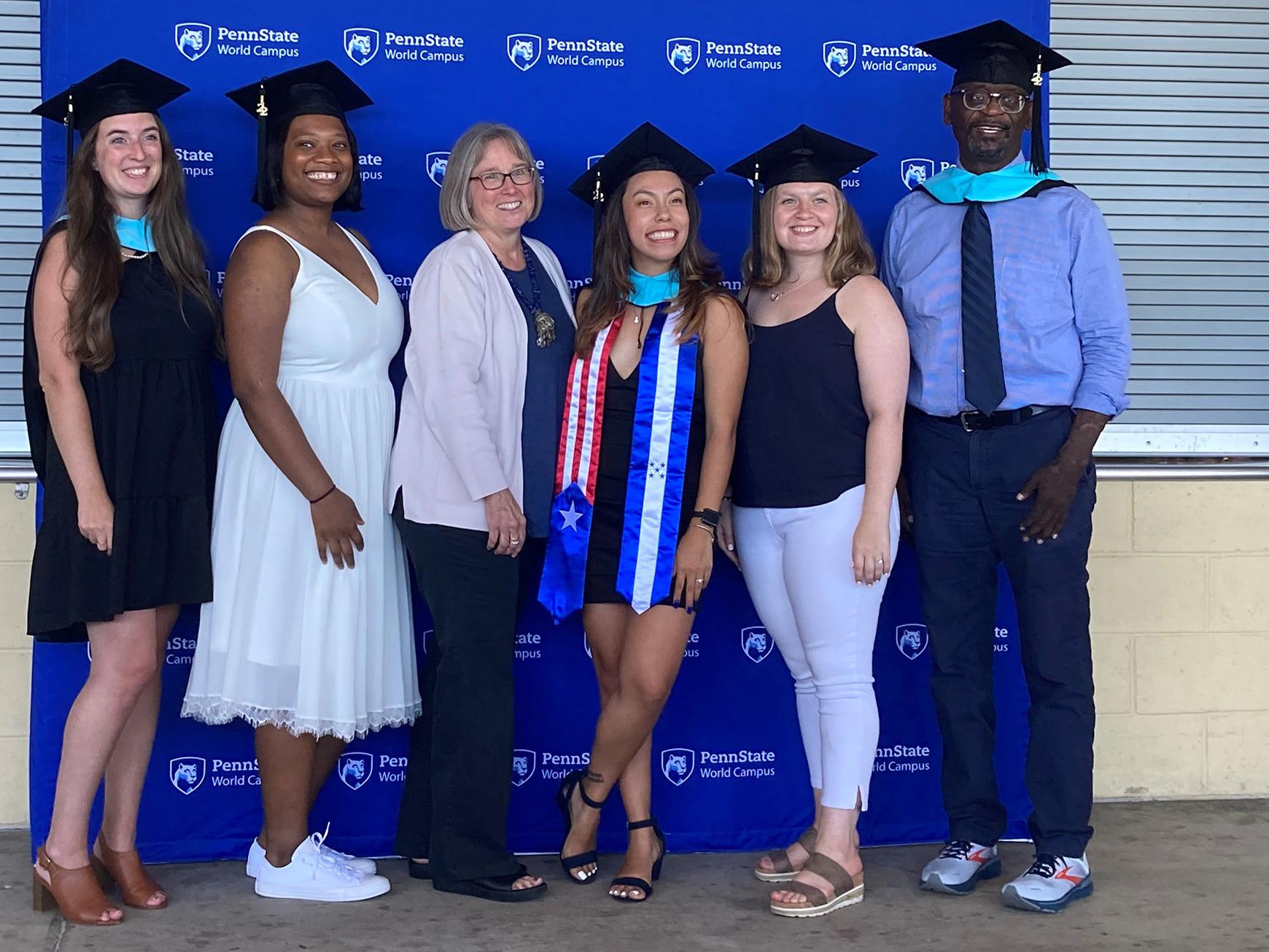 Students and a faculty member from the Master's in higher education pose for a photo in front of a Penn State World Campus banner