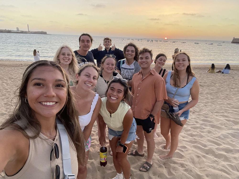 A group of college students stands on the beach in front of the ocean and a sunset in Cadiz, Spain