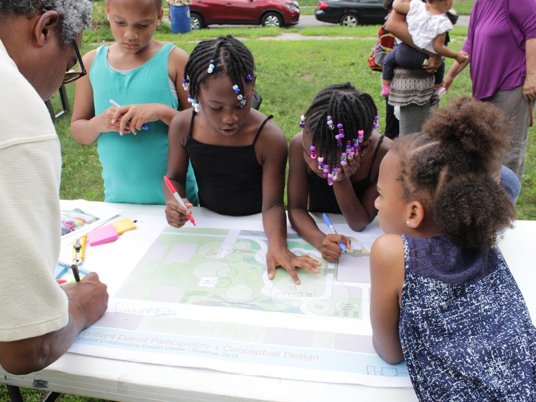 A man writing on landscape plans with children surrounding him. 