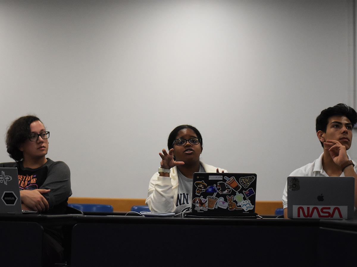 A student asks a question while the two students to her right and left listen