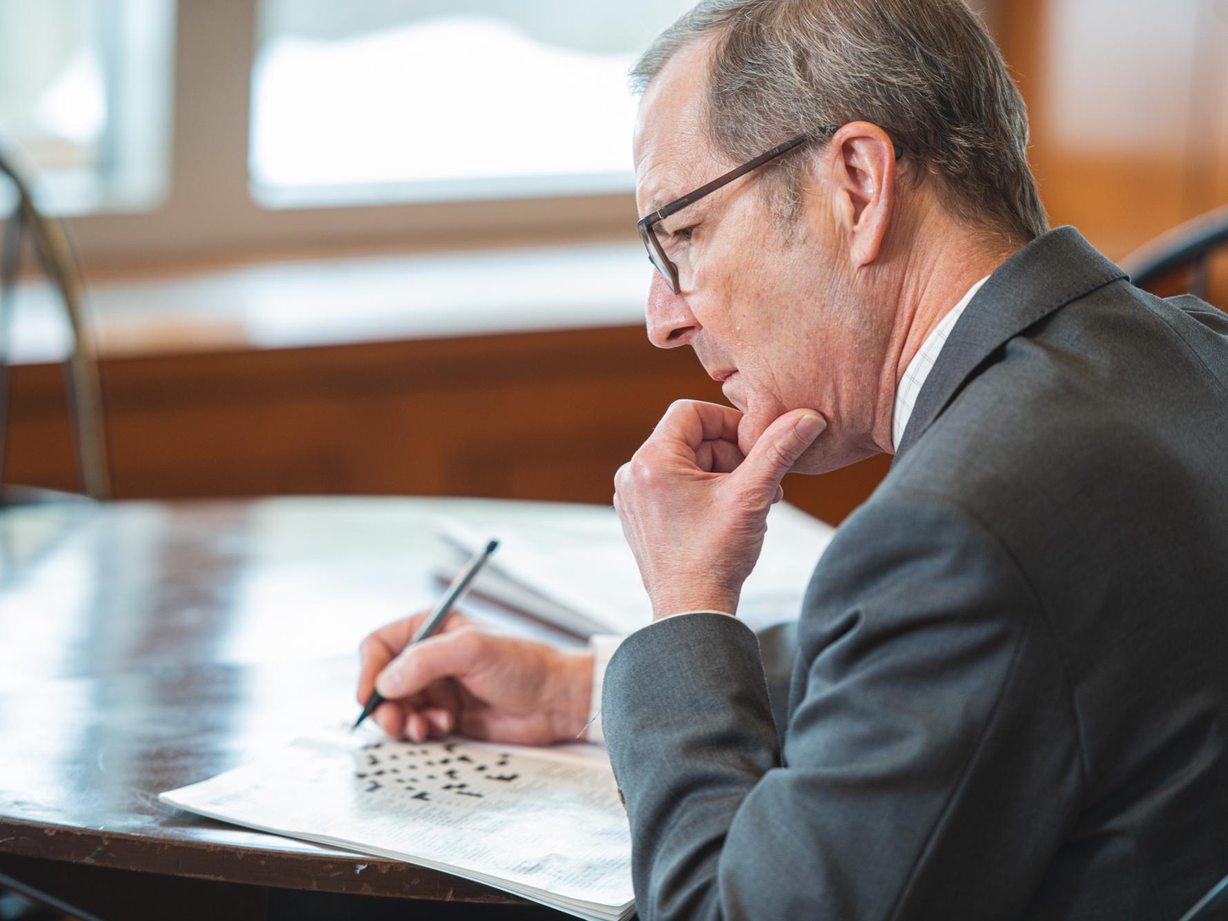 Charles Whiteman, dean of the Smeal College of Business, sits at a table with a thoughtful expression as he works on a crossword puzzle