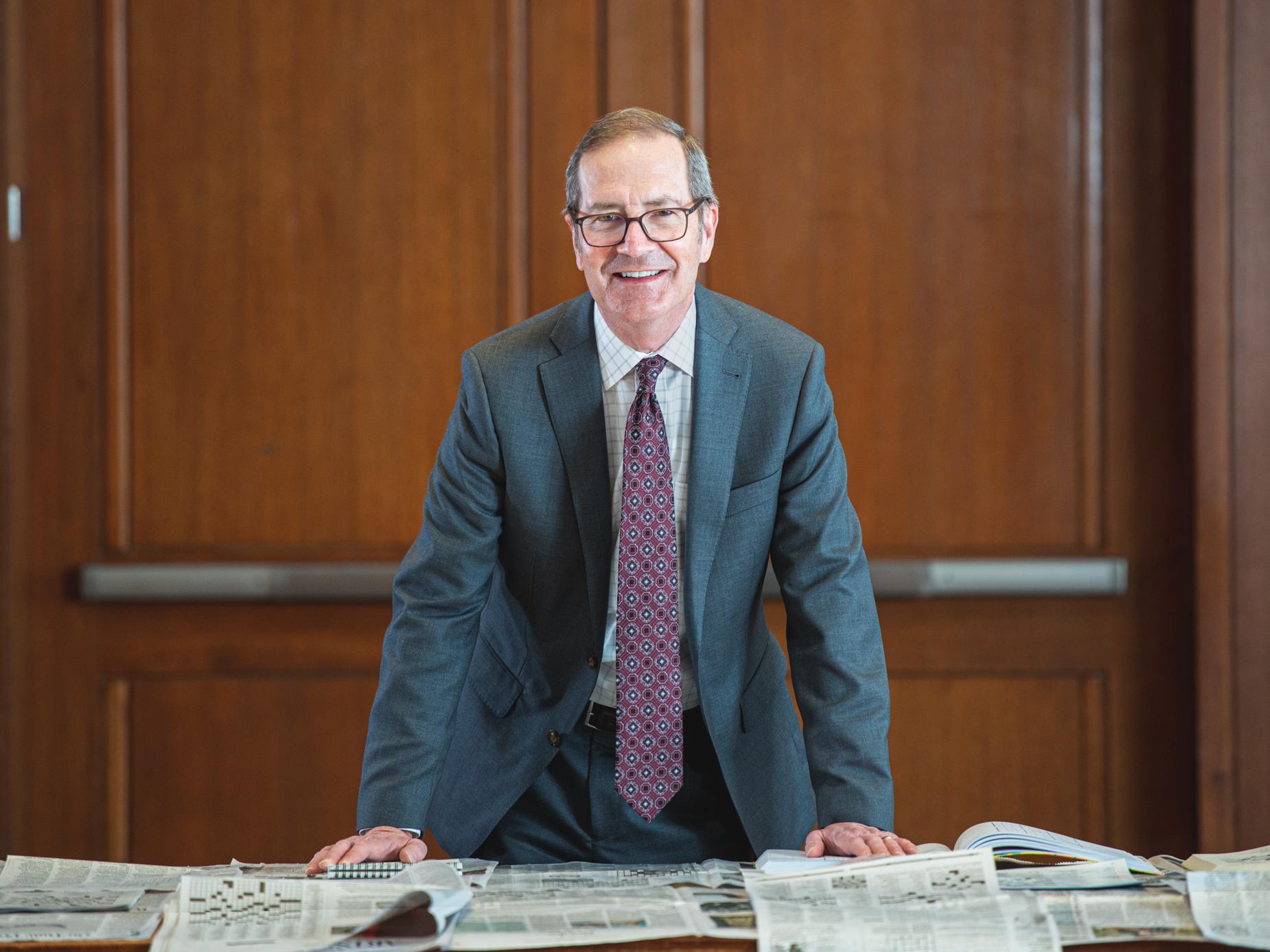 Charles Whiteman, dean of the Smeal College of Business, stands smiling behind a desk covered in newspapers