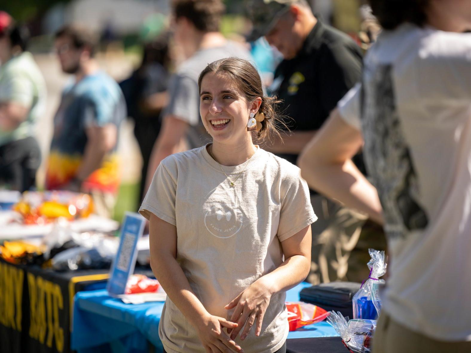 A female student smiles while standing at a table during the Penn State Behrend Discovery Fair.