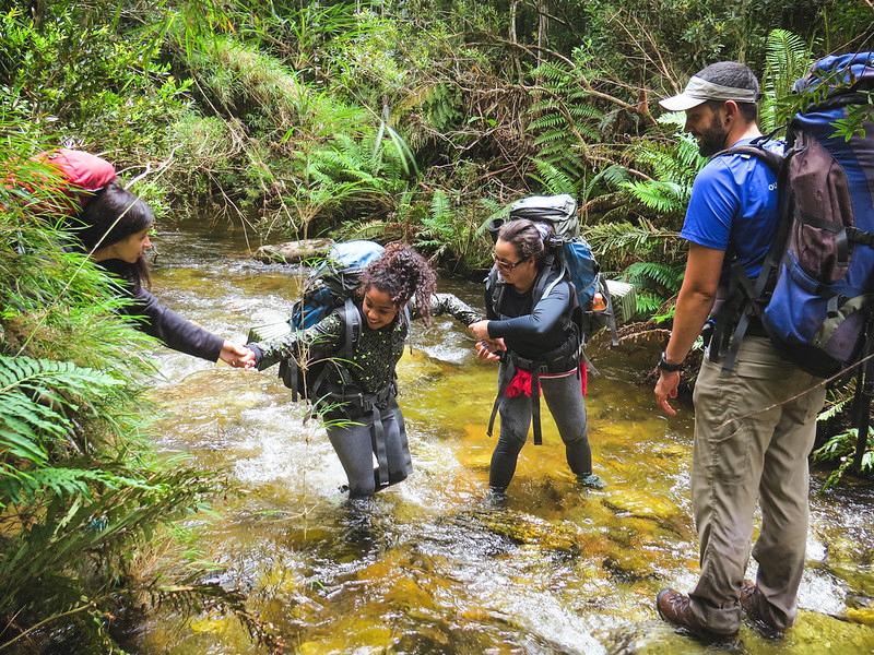 Outward Bound students help each other cross a stream in the rainforest